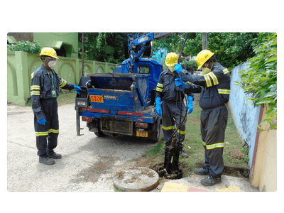 Sanitation workers in PPE beside a mechanized desludging vehicle at a manhole